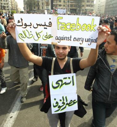 In Cairo’s Tahrir Square in February 2011, a man joins protestors calling for the ouster of Hosni Mubarak’s long-term regime, while holding a sign praising Facebook. Voices once crediting social media’s role in the revolution have grown quieter since. Photo by Khaled Desouki via Getty Images.